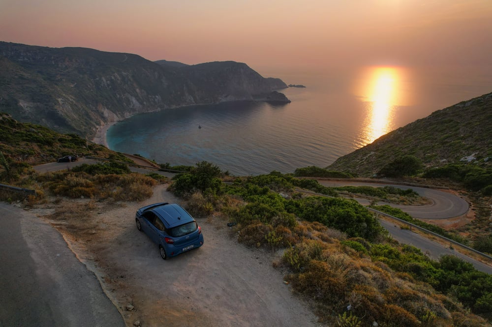 Een geparkeerde auto bij een baai tijdens een zonsondergang in Griekenland