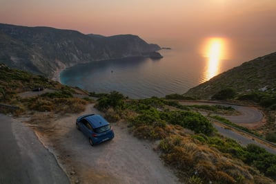Een geparkeerde auto bij een baai tijdens een zonsondergang in Griekenland