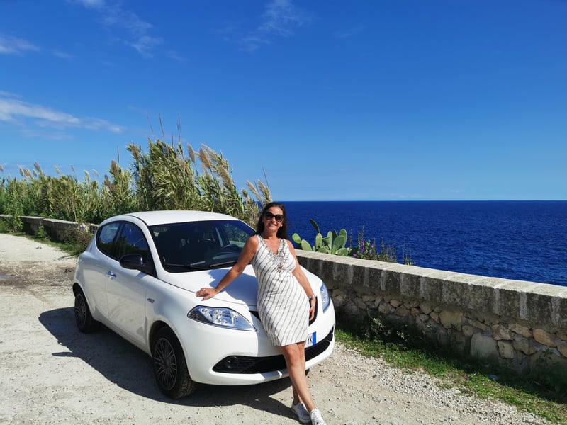 Witte auto met vrouw langs een kustweg in Italië