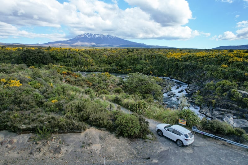 Uitzichtpunt over rivier, rotsen en groene bergen en een witte auto