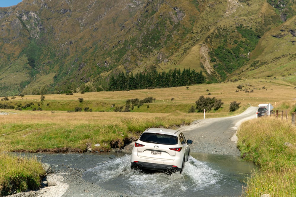 Witte auto doorwaadt een rivier bij Wanaka Mount Iron, Mieuw-Zeeland