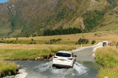 Witte auto doorwaadt een rivier bij Wanaka Mount Iron, Mieuw-Zeeland